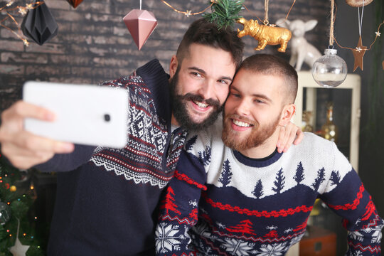 Portrait of happy gay couple taking selfie with smartphone at Christmas time at home