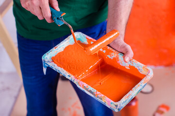 Close-up of man holding paint tray with orange paint