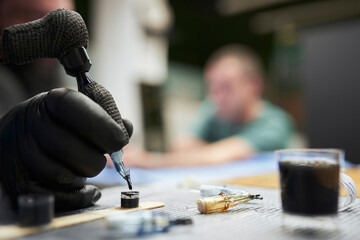 Hand of male artist dipping tattoo machine in ink on table