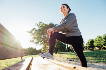 Female jogger stretching her leg on bench in park