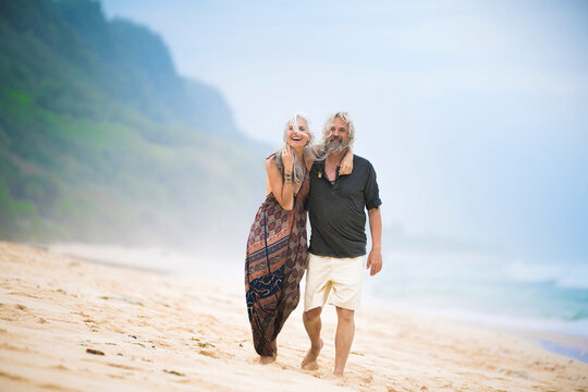 Happy senior hippie couple strolling side by side on the beach