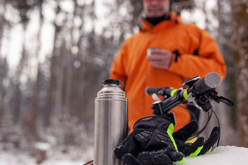 Man having a break from mountainbike trip in winter forest having a hot drink
