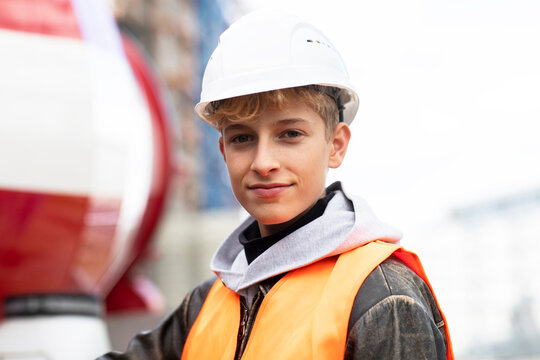 Confident male teenage trainee wearing hardhat and reflective clothing at construction site