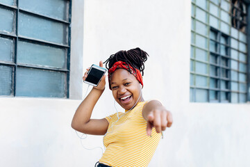 Portrait of excited young woman listening music with headphones and earphones in front of white wall