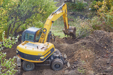 Yellow excavator begins to dig a pit