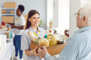 Positive volunteer woman giving a food donation box to a pensioner at a social assistance center or...