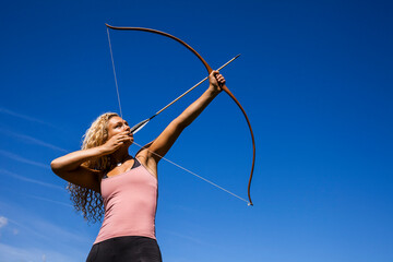 Archeress aiming with bow against blue sky