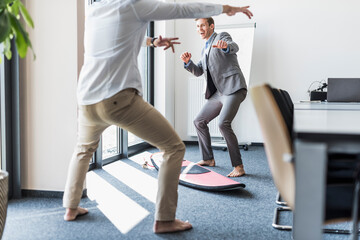 Two playful colleagues with surfboard in office
