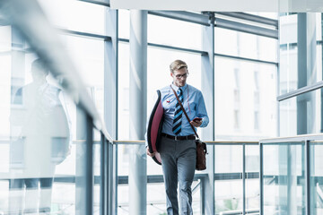 Businessman with cell phone carrying surfboard in office