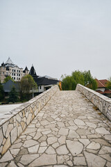 A young girl stands on a stone old bridge and enjoys the views of nature and buildings. Hotel Moskva - Moscow in Bijeljina - small town in Bosnia and Herzegovina. Stanisici Ethno Village.