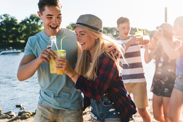 Group of happy friends walking at the riverside toasting with drinks