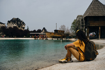 A young woman travels with one backpack. A girl with dreadlocks sits near a turquoise lake and...