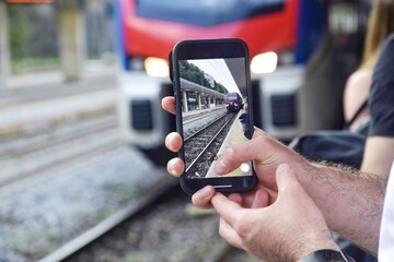 A man films on his phone as a train approaches the station.