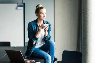 Smiling businesswoman sitting on table in office having a coffee break