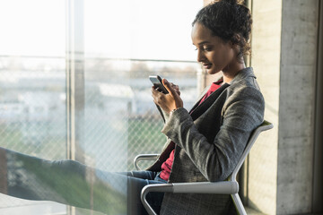 Young businesswoman using cell phone at the window in office
