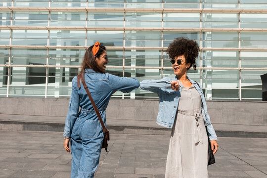 Smiling friends greeting with elbow bumps while standing on rooftop in city
