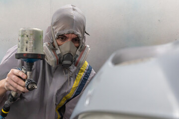 Auto mechanic in protective gear painting a car