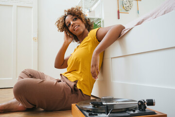 Young woman listening to music with headphones and record player at home