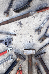 Old working tools on a concrete surface, top view. Hammers, flat file, tin snips, adjustable wrench...