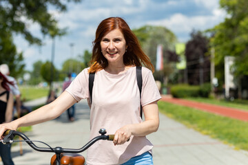 Obraz premium Pretty Woman walking and holding her bike next to her in the park 