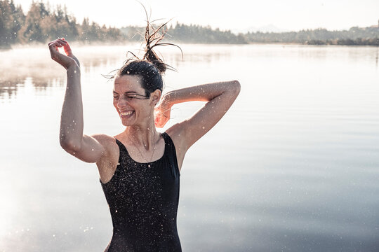 Cheerful woman wearing black swimsuit at a lake at morning mist