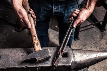 Knife maker holding pliers and hammer on anvil