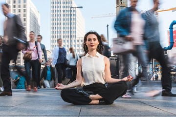 Young businesswoman practising yoga in the city at rush hour, Berlin, Germany