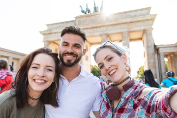 Portrait of three happy friends taking selfie with cell phone in front of Brandenburger Tor,...