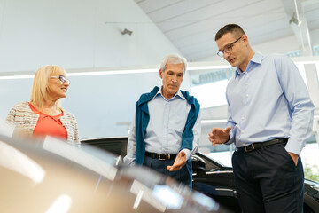 Senior couple couple talking with salesperson in car dealership