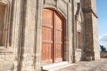 Fototapeta premium Old wooden door on a weathered stone Church of Timios Prodromos facade at Vouni village. Limassol District, Cyprus