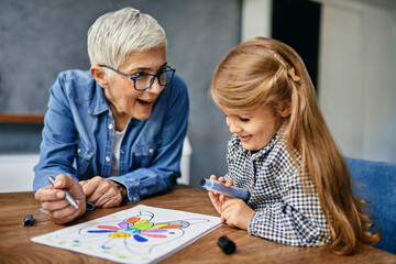 Grandmother and granddaughter sitting at table, painting colouring book