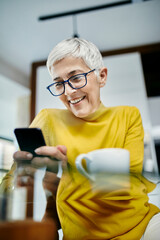 Senior woman drinking coffee, checking text messages on her smartphone