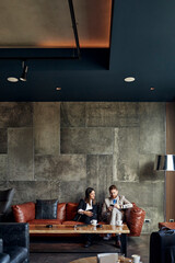 Businessman and businesswoman sitting on couch in hotel lobby sharing smartphone