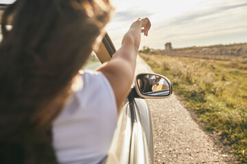 Young woman pointing towards cloudy sky while sitting in car