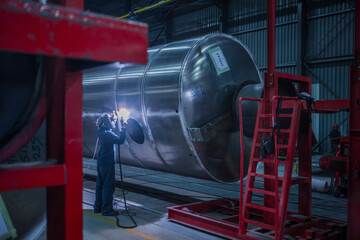 Man welding large steel tank in factory