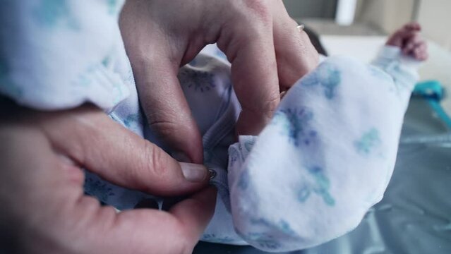 Parent&rsquo;s hands tenderly snap a tiny button on the baby&rsquo;s outfit, emphasizing the detailed care involved in dressing a newborn. hands and clothing, symbolizing love and protection