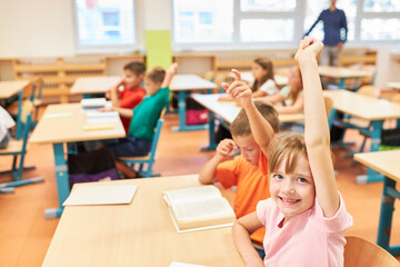 Happy schoolgirl raising hand in class