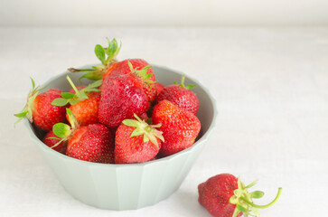 Ripe red strawberries in a green bowl on a gray table. Concept of summer food. Horizontal orientation. Selective focus. Copy space
