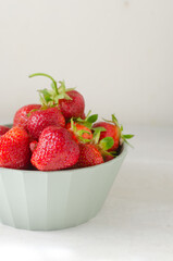 Ripe red strawberries in a green bowl on a gray table. Concept of summer food. Vertical orientation. Selective focus.