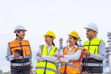 Happy diverse group of petrochemical engineers working together with digital tablet with petroleum oil refinery in industrial estate background. Engineers at power plant energy industry manufacturing.