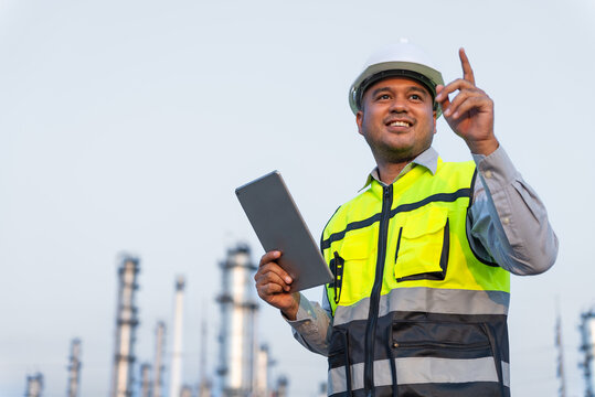 Happy handsome Asian man petrochemical engineer working with digital tablet. He going through routine checks at petroleum oil refinery in industrial estate. Engineers at industry manufacturing.