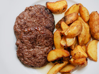 Beef burger and potato wedges on a white plate. Simple plain meal. Dinner with meat product and vegetable.