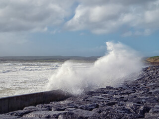 The ocean is rough and the high waves are crashing against the rocks. The sky is cloudy and the water is a deep blue color. Storm weather.