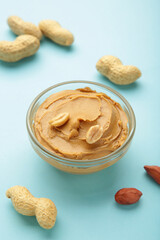 Bowl of peanut butter and peanuts on blue background. Creamy peanut pasta in small bowl.
