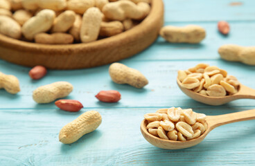 Fresh healthy peanuts in bowl and spoon on blue wooden background.