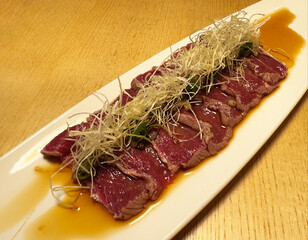 Tuna tartare served in white plate and isolated on yellow table background. Healthy food. Appertizer. Tuna starter