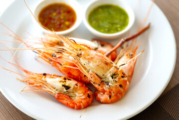 Grilled prawns with two different sauce to dipping, green sauce seafood and sweet red chili sauce. Grilled prawns in dish with natural light from window, close up food image.