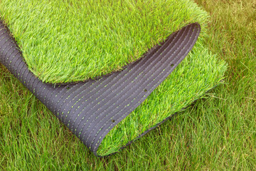 The roll of synthetic grassyard surface for gardening. Decorative lawn cover with vibrant green color. The difference between the natural and artificial grass.