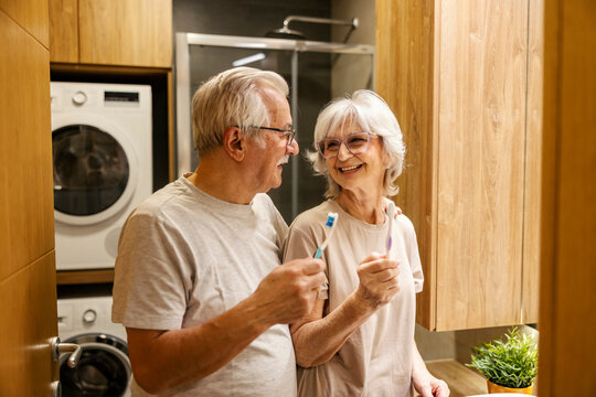 Happy senior couple standing in bathroom with toothbrushes in hands and smiling at each other. - Powered by Adobe