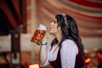 Young, beautiful woman in a traditional Oktoberfest dirndl drinks a mass of beer in the beer tent at the Oktoberfest